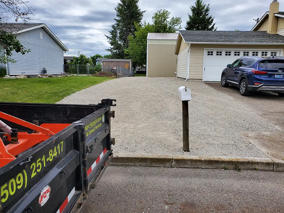 A newly installed light gray gravel driveway and parking area next to a residential garage.