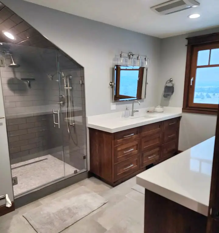 Custom bathroom remodel in a sloped-ceiling space featuring a walk-in glass shower, subway tile, and high-end wood cabinetry.