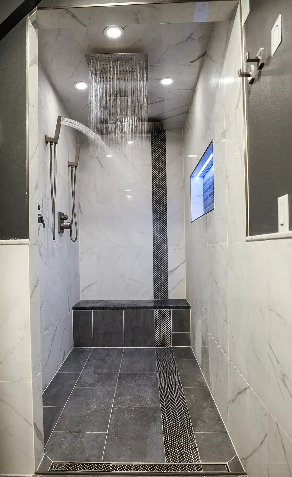 Luxury bathroom remodel showing a tiled walk-in shower with dual showerheads, a built-in seat, and modern recessed lighting.