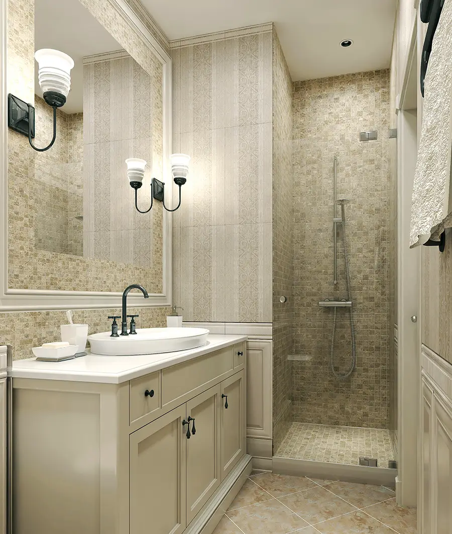 A modern, beige-toned bathroom with a large mirror, white sink, countertop with toiletries, paneled cabinets, wall sconces, and a glass-enclosed shower with a rainfall showerhead and tiled walls and floor.